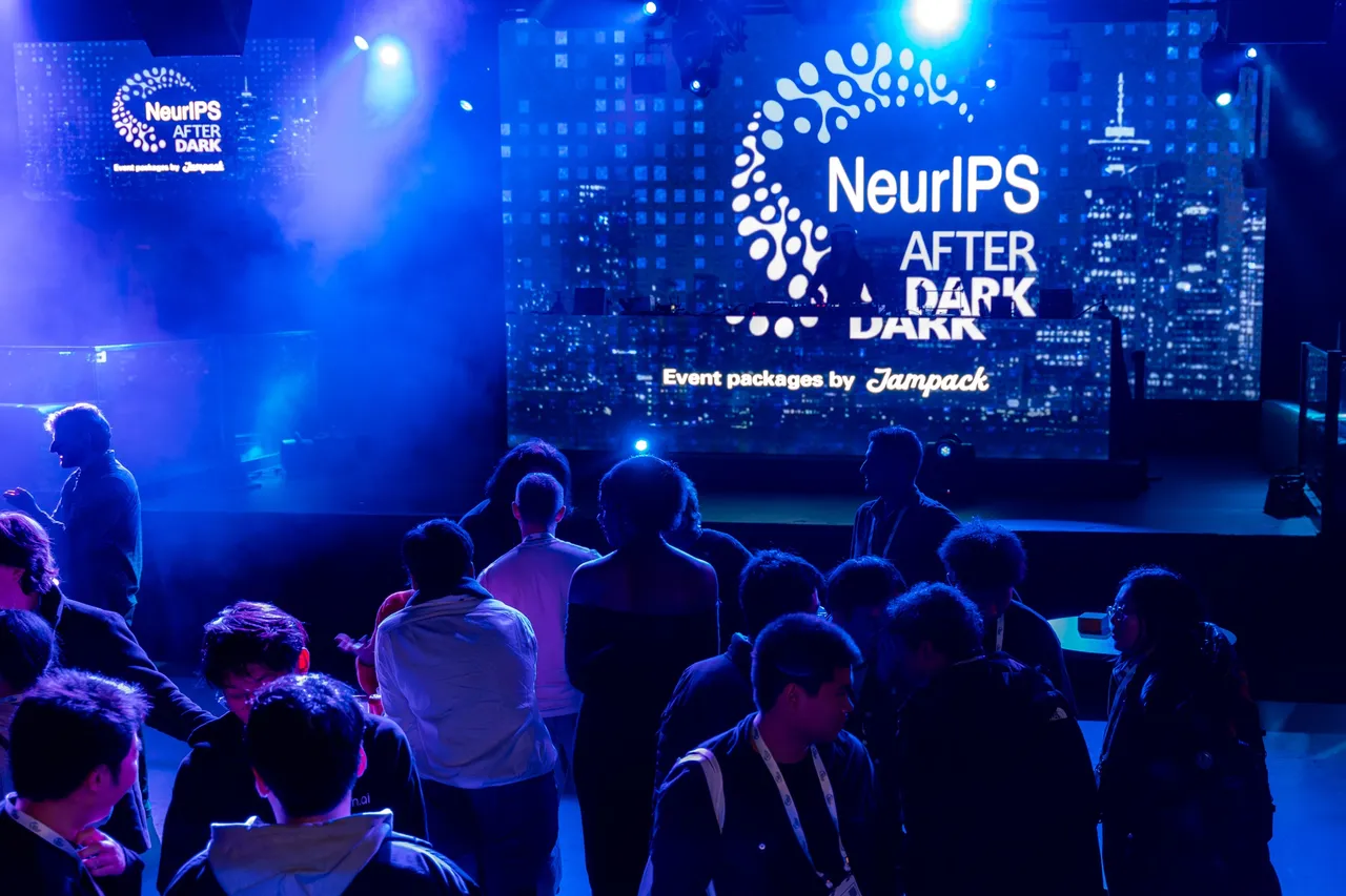 Conference attendees filling the floor of an evening event, a full-width illuminated screen behind them.
