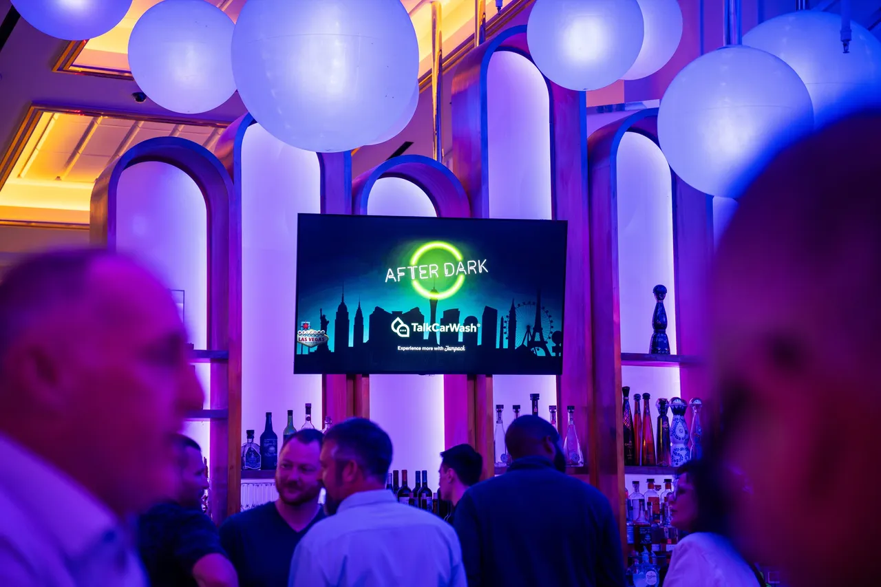 Guests talking over drinks at a hosted evening reception, under hanging globe lights in a columned room.